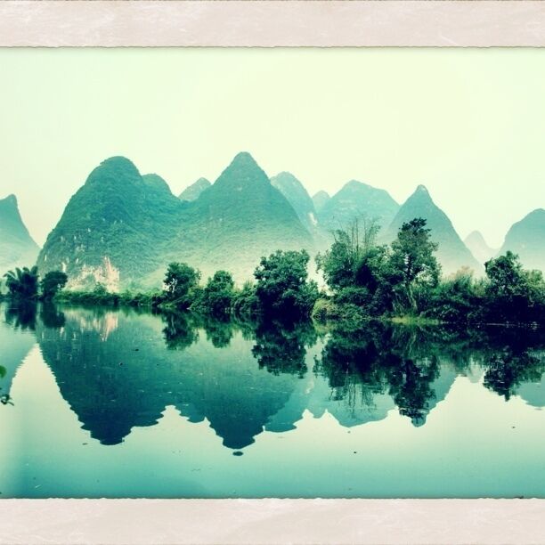 A calm lake with reflections of green mountains and trees.