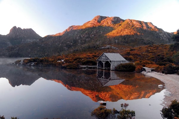 Un abri à bateaux en bois, situé sur un lac paisible, avec une montagne en arrière-plan.
