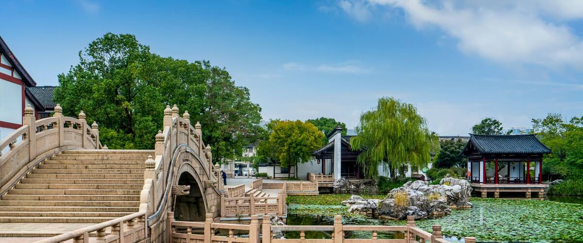 A stone bridge, a pond with lily pads, and traditional buildings.