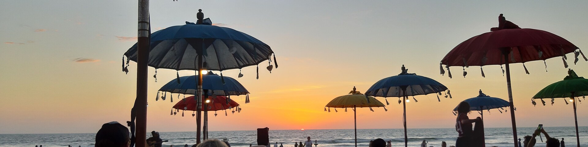 Una playa con sombrillas de colores y pufs al atardecer.