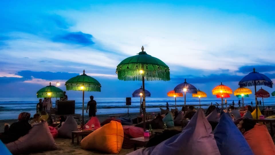 A beach with colorful umbrellas and bean bags under a twilight sky.