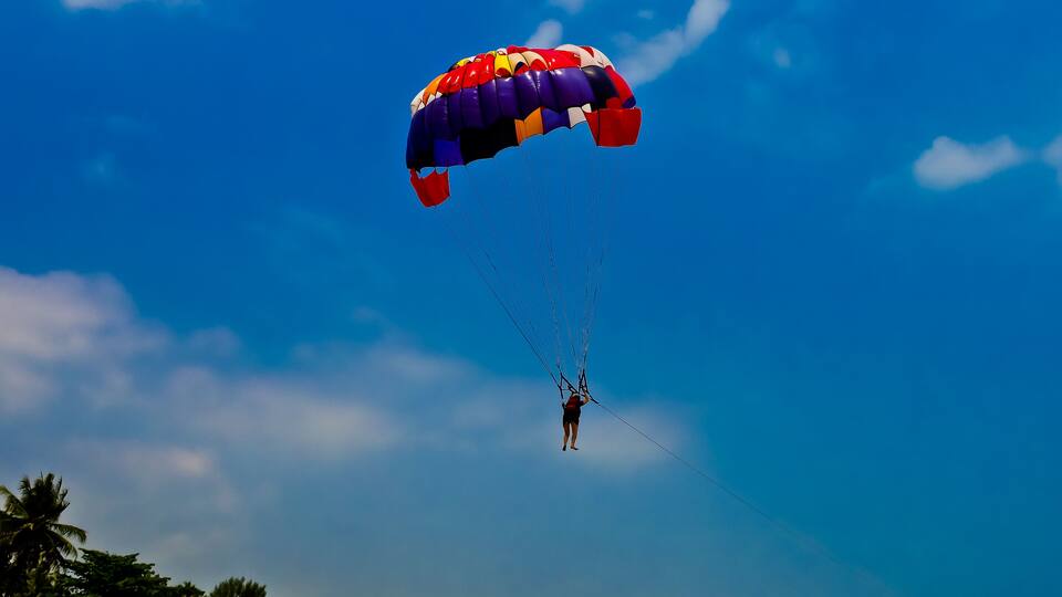 A person skydiving with a colorful parachute against a clear blue sky.