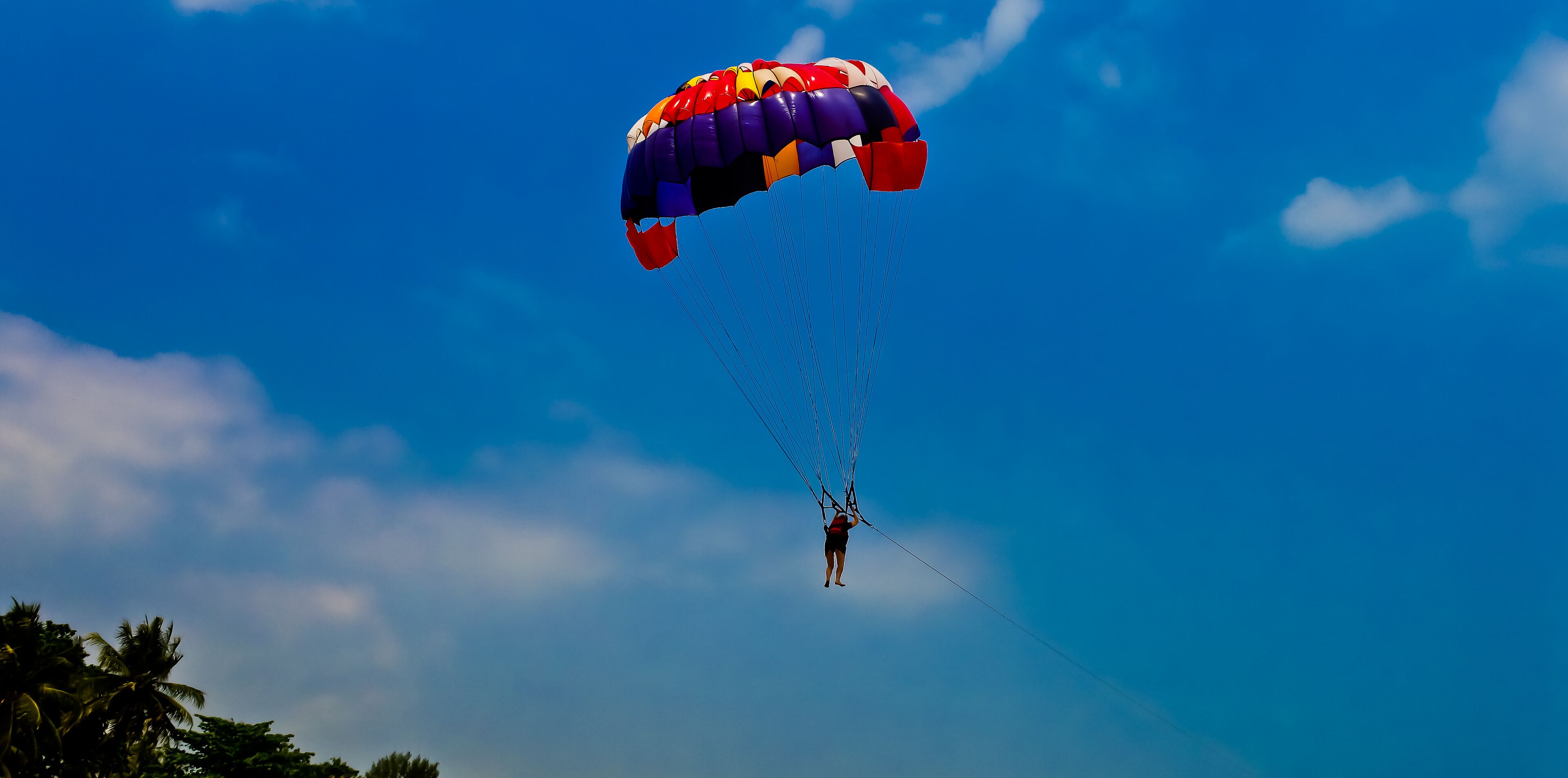 A person skydiving with a colorful parachute against a clear blue sky.