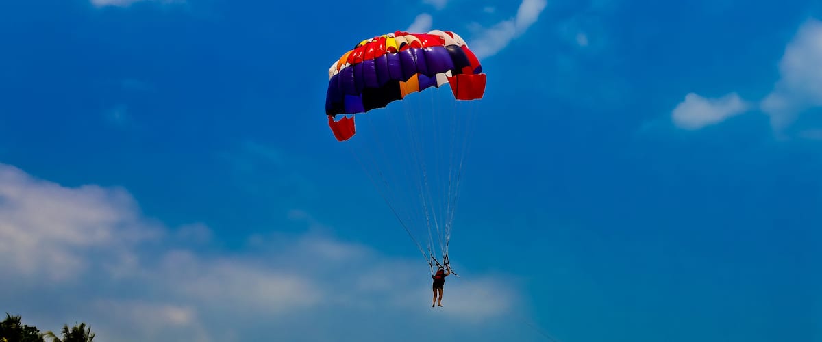 A person skydiving with a colorful parachute against a clear blue sky.