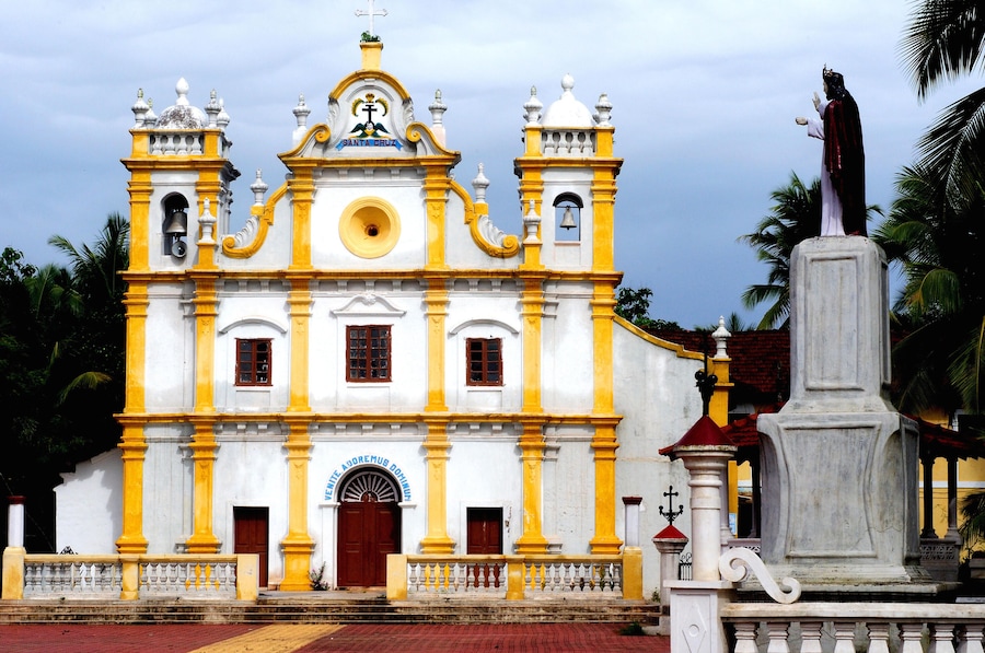 A white and yellow church with a bell tower and a statue in front.