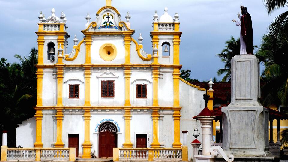 A white and yellow church with a bell tower and a statue in front.