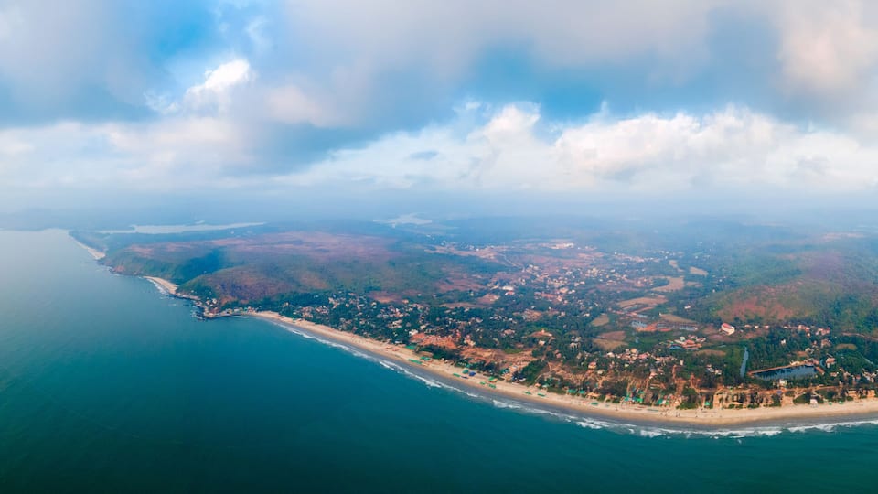 An aerial view of a coastal town with a beach, dense forest, and a large body of water.
