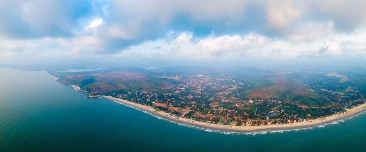 An aerial view of a coastal town with a beach, dense forest, and a large body of water.