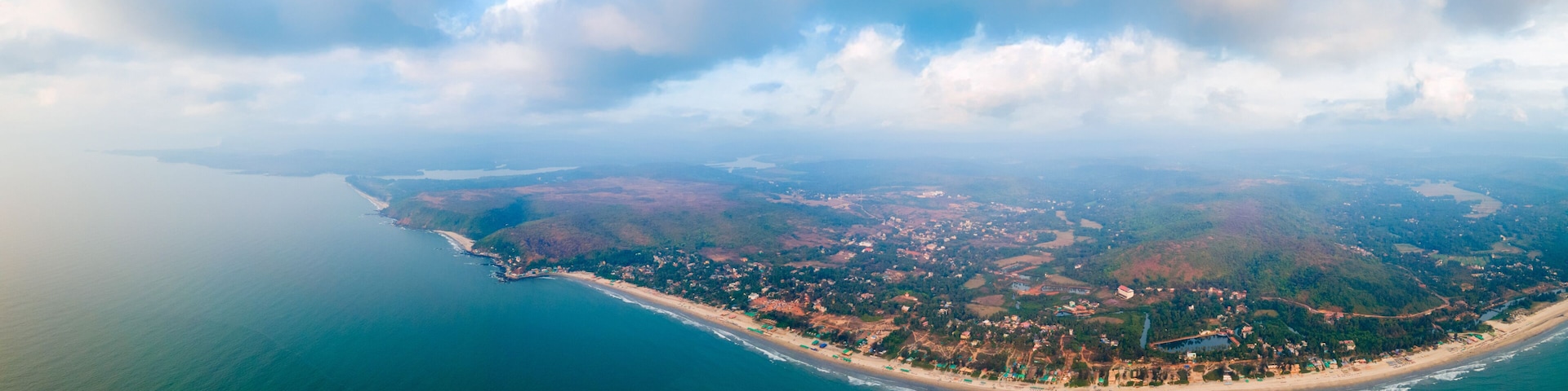 An aerial view of a coastal town with a beach, dense forest, and a large body of water.