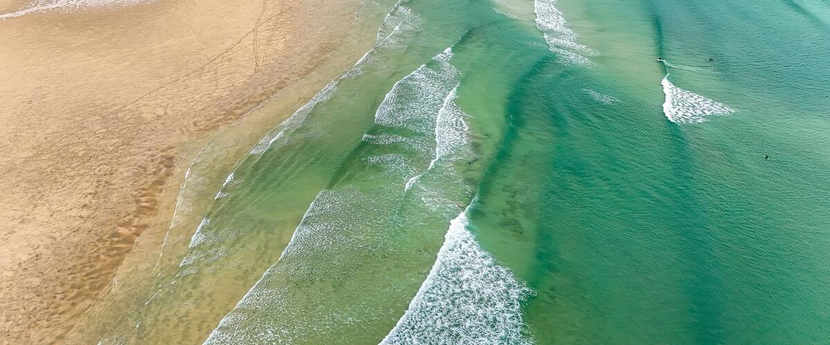 A coastal landscape with clear green waters, sandy beaches, and gentle waves.
