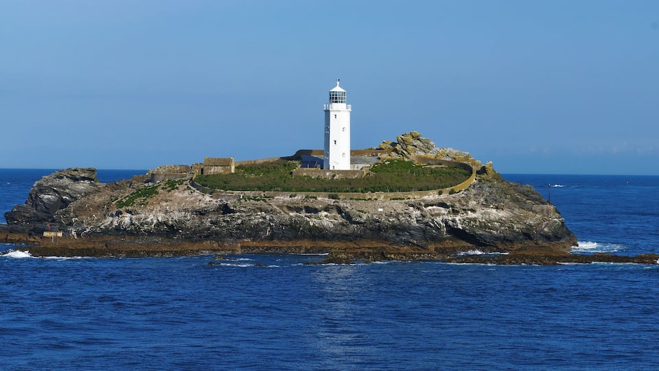 A white lighthouse on a rocky island surrounded by deep blue ocean.