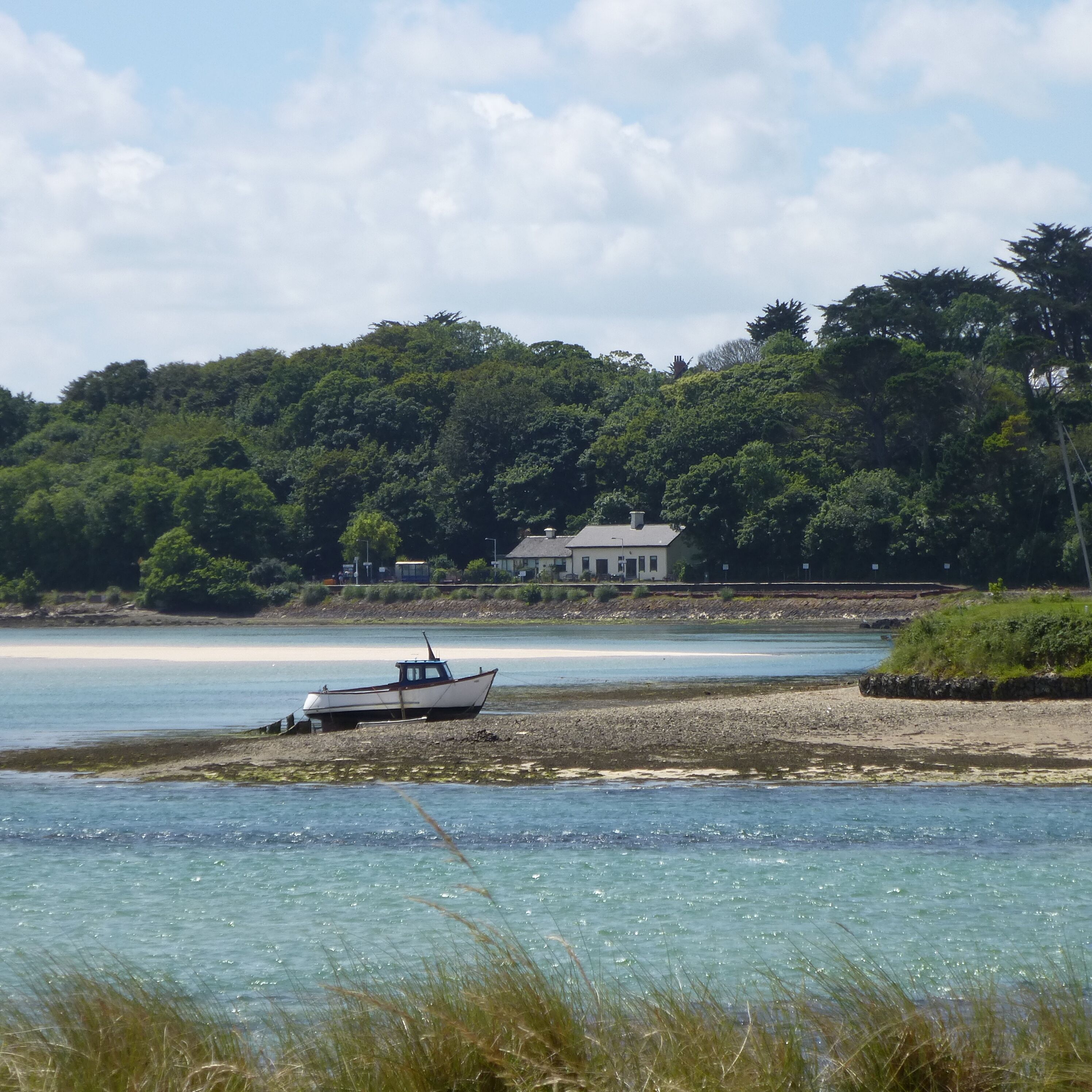 A boat on a pebbly shore with a house and forest in the background.