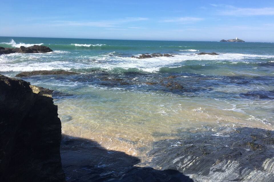 A rocky coastline with waves crashing against the shore and a lighthouse in the distance.
