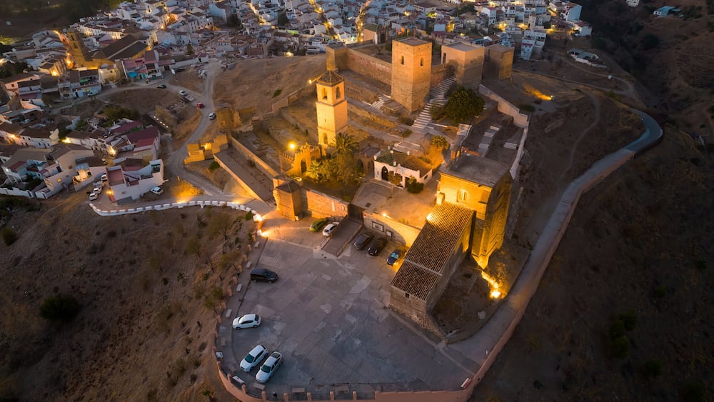 An aerial view of a historic walled town with prominent towers and a central square.