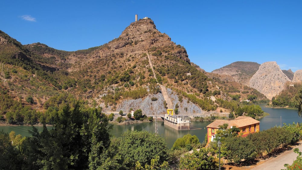 A mountainous landscape with a dam, a body of water, and a small building.