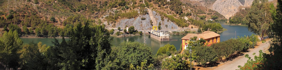 Eine Berglandschaft mit einem Stausee und einem kleinen Gebäude.