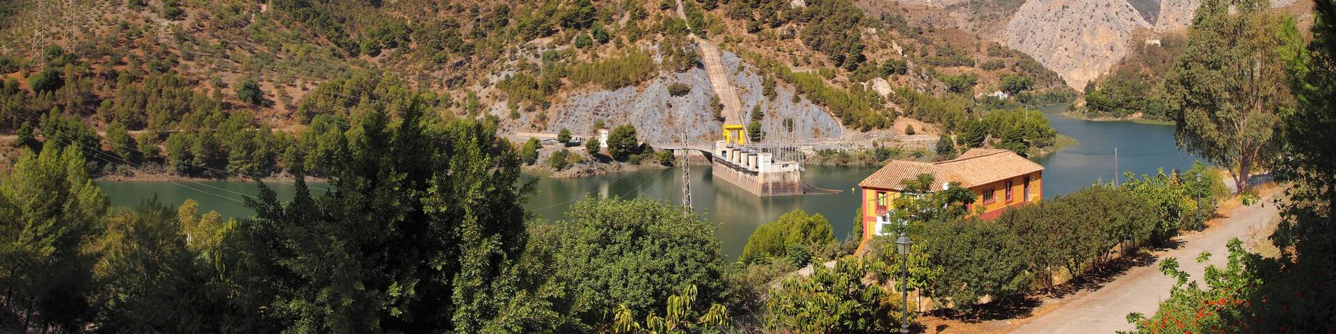 A mountainous landscape with a dam, a body of water, and a small building.
