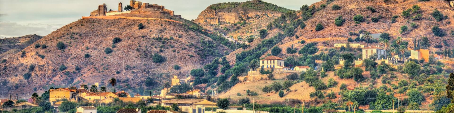 A mountainous landscape with historic buildings, including a fortified structure and residential houses.