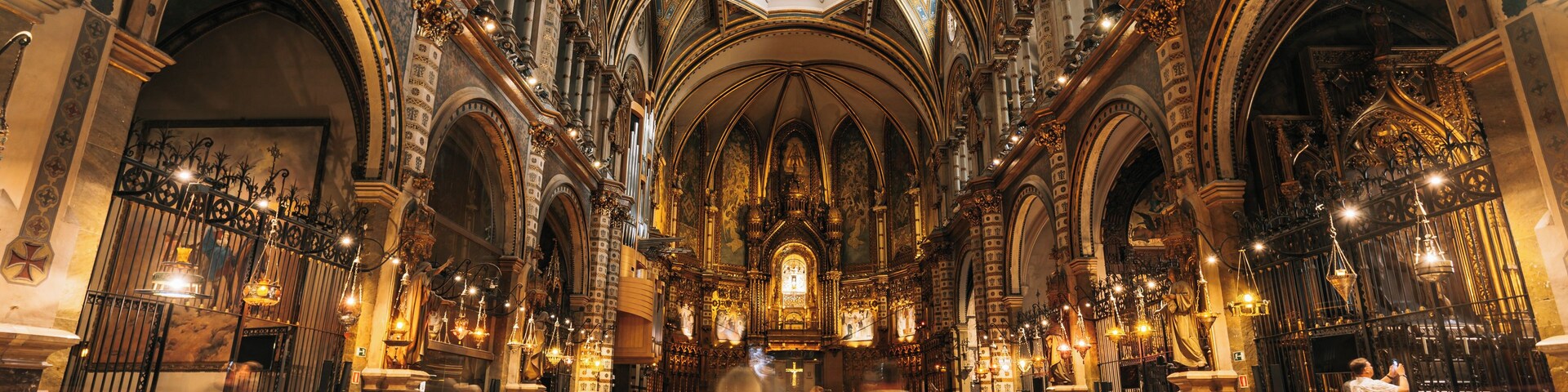 Interior de igreja ornamentado, com altos tetos abobadados, intrincados trabalhos em madeira e fileiras de bancos.