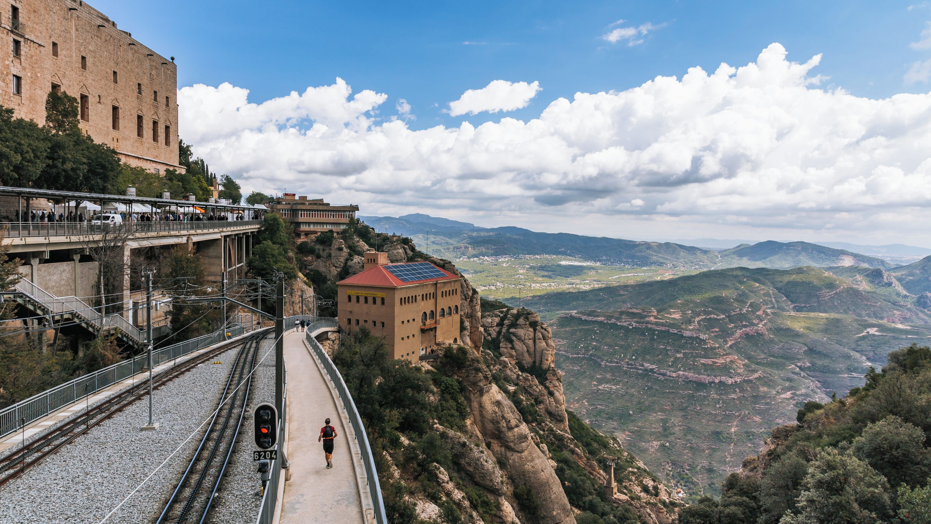 A mountain railway with a pedestrian bridge, a historic building, and a valley view.