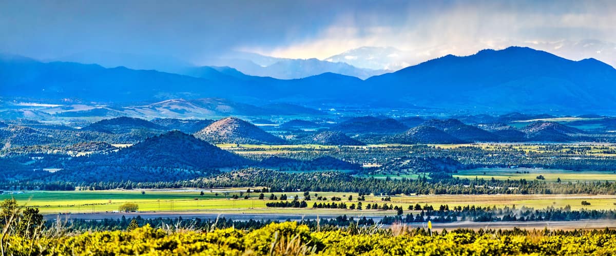 A mountainous landscape with a valley, fields, and a river.