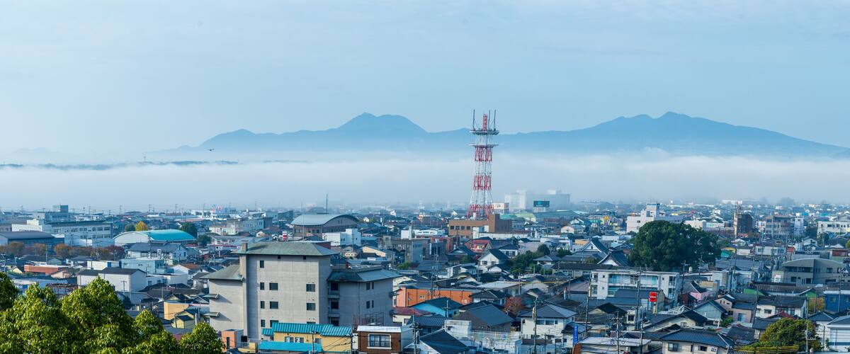 A cityscape with a prominent communication tower, dense urban buildings, and a mountain range in the background.