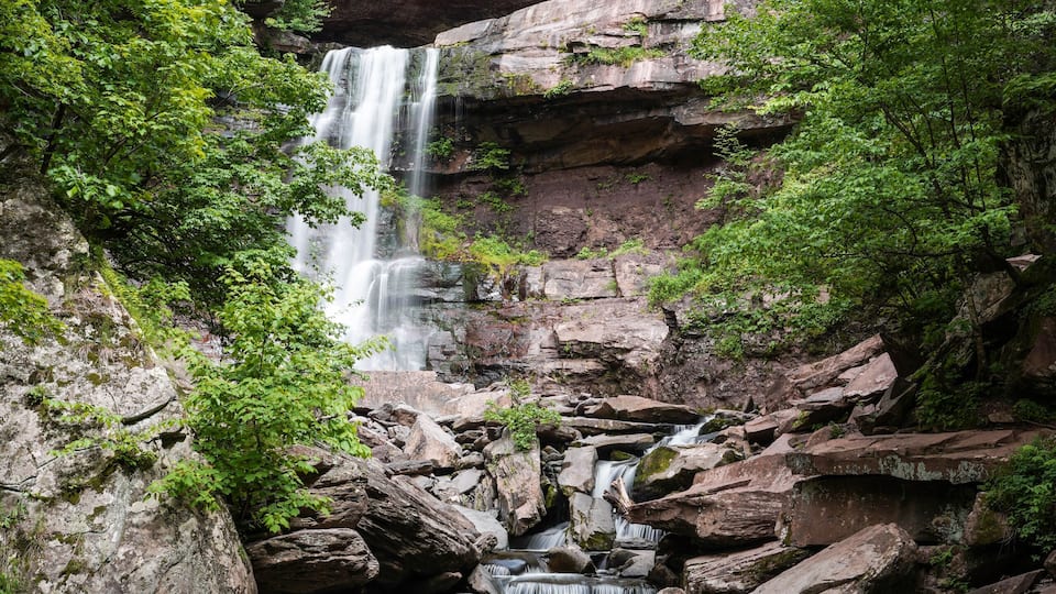 A multi-tiered waterfall surrounded by lush greenery and rocky terrain.