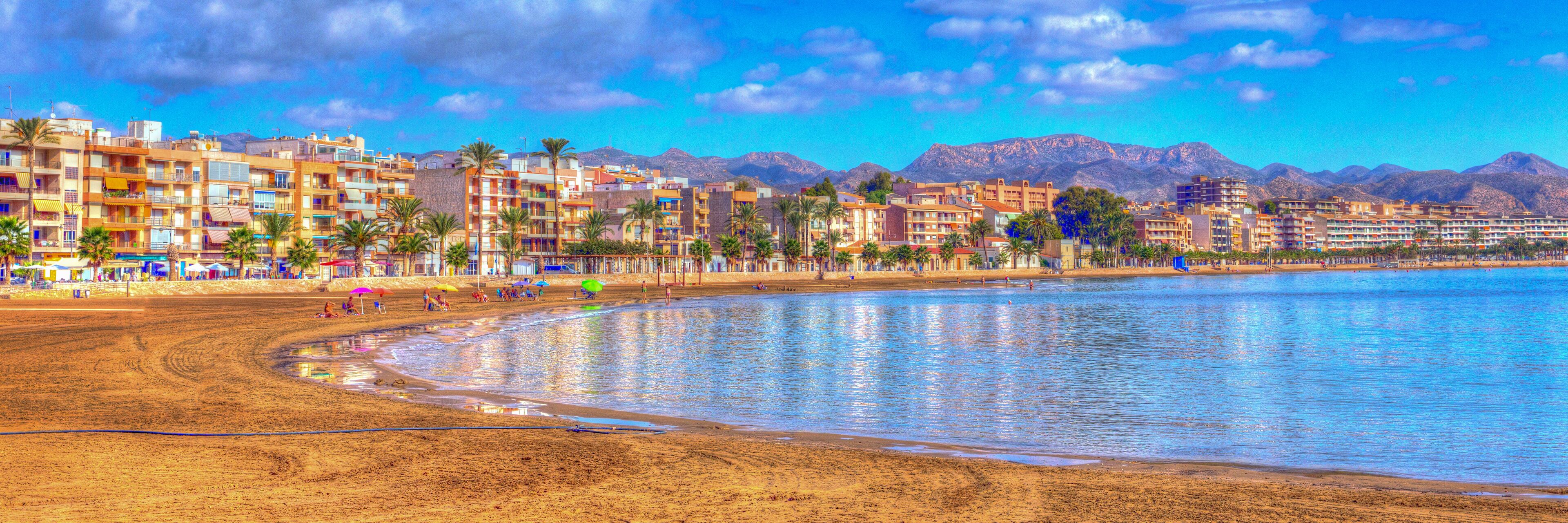 A beach with buildings and mountains in the background.