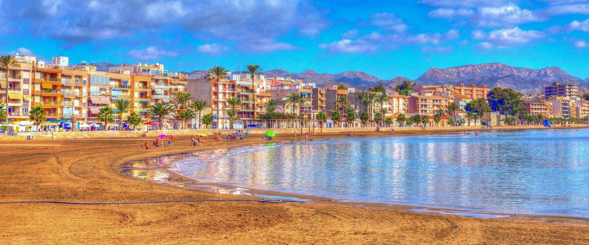 A beach with buildings and mountains in the background.
