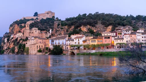 Miravet, Spain, a riverside village with a castle on a hill at dusk.