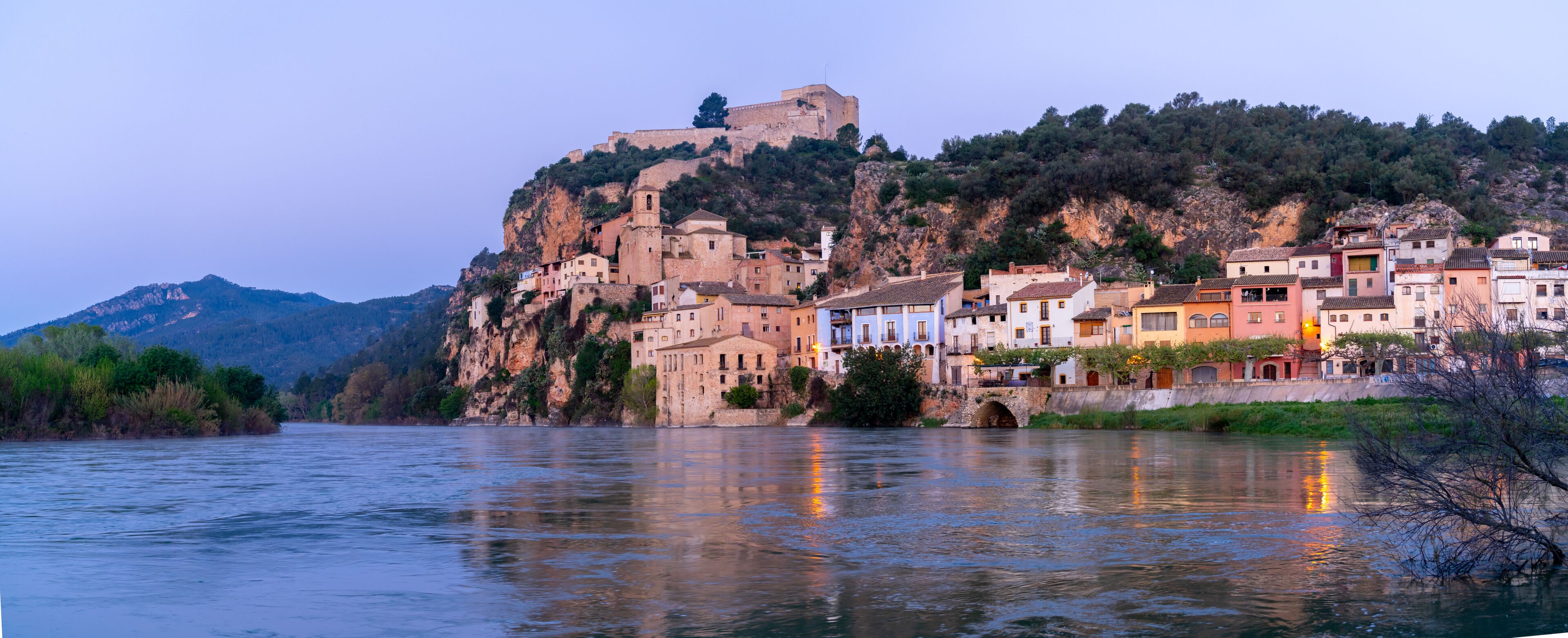 A river with buildings on a hillside and a castle on top.