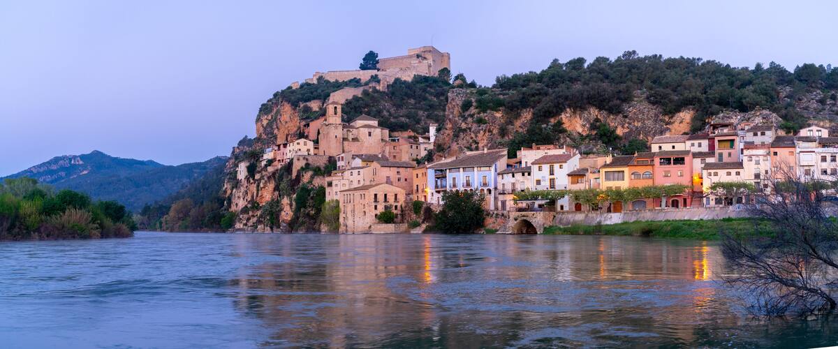 A river with buildings on a hillside and a castle on top.