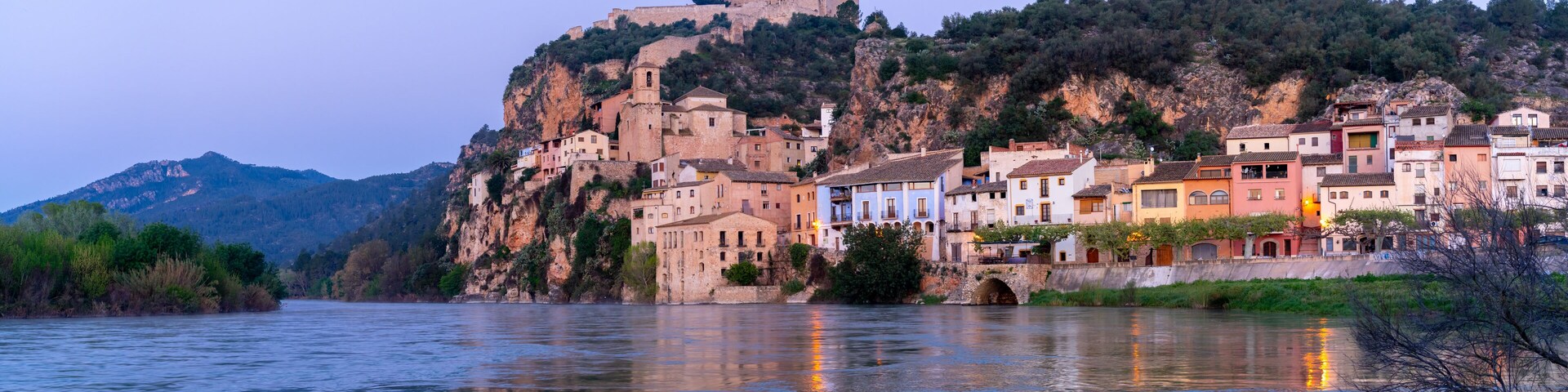A river with buildings on a hillside and a castle on top.