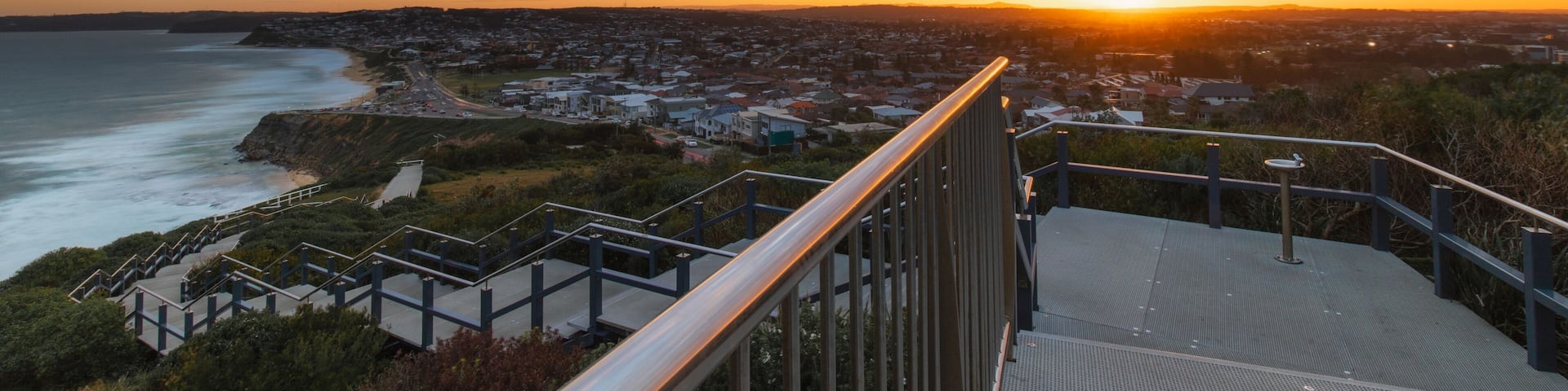 A coastal sunset view with a staircase leading down to the beach.