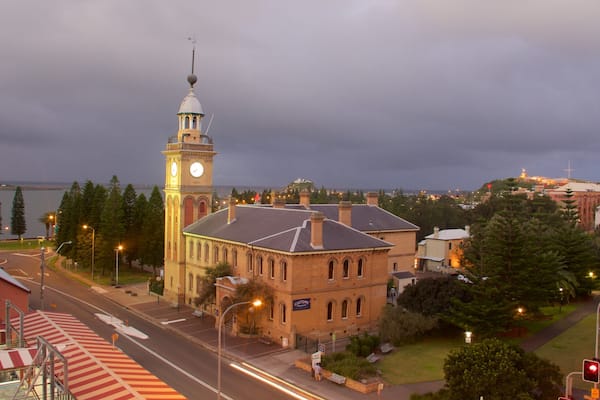 A historic building with a clock tower, a waterfront, and a stormy sky.