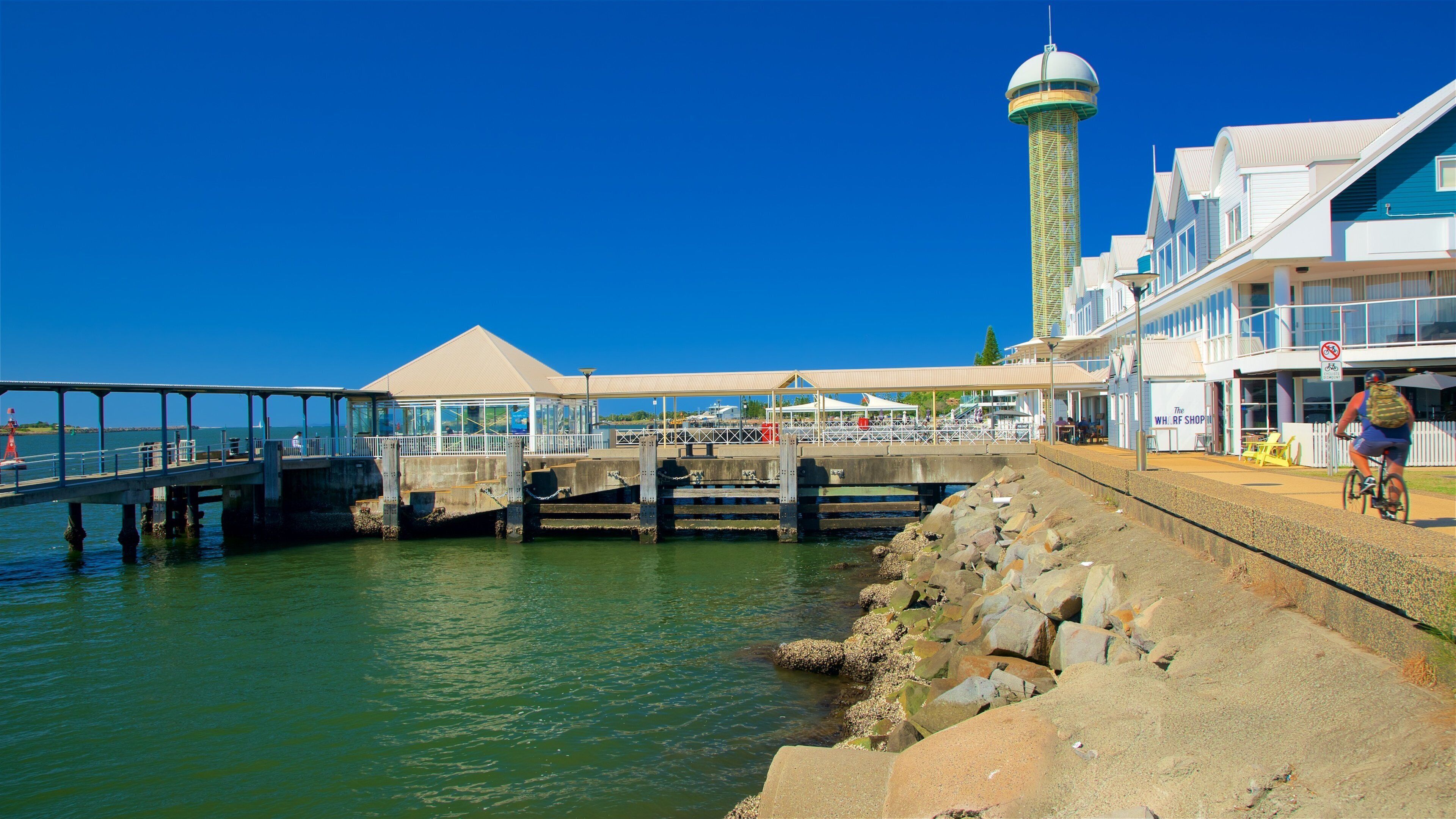 Un molo costiero con un faro, una passerella coperta e un ristorante sul lungomare.
