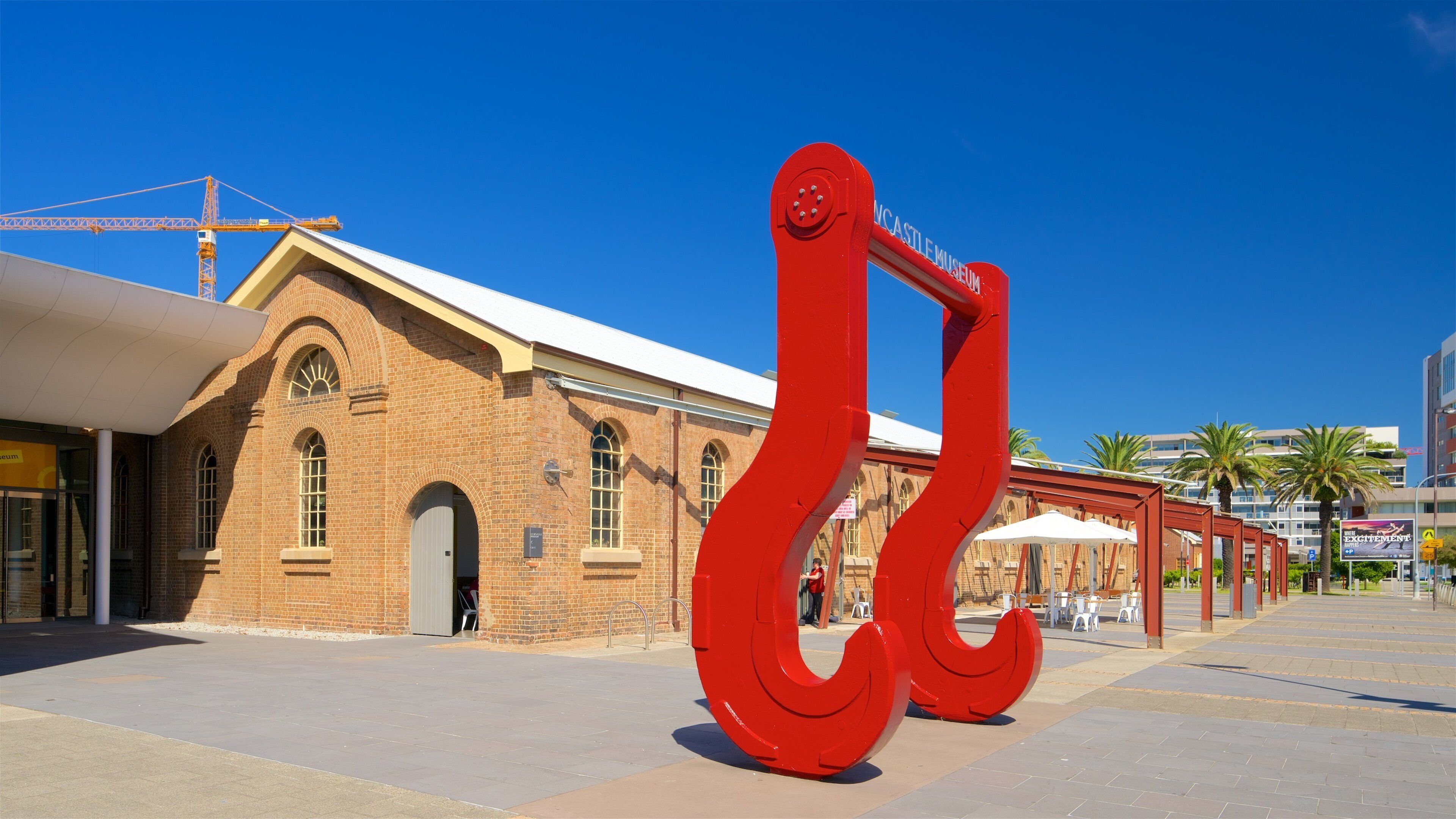 Una escultura roja frente a un edificio histórico, con una grúa al fondo.