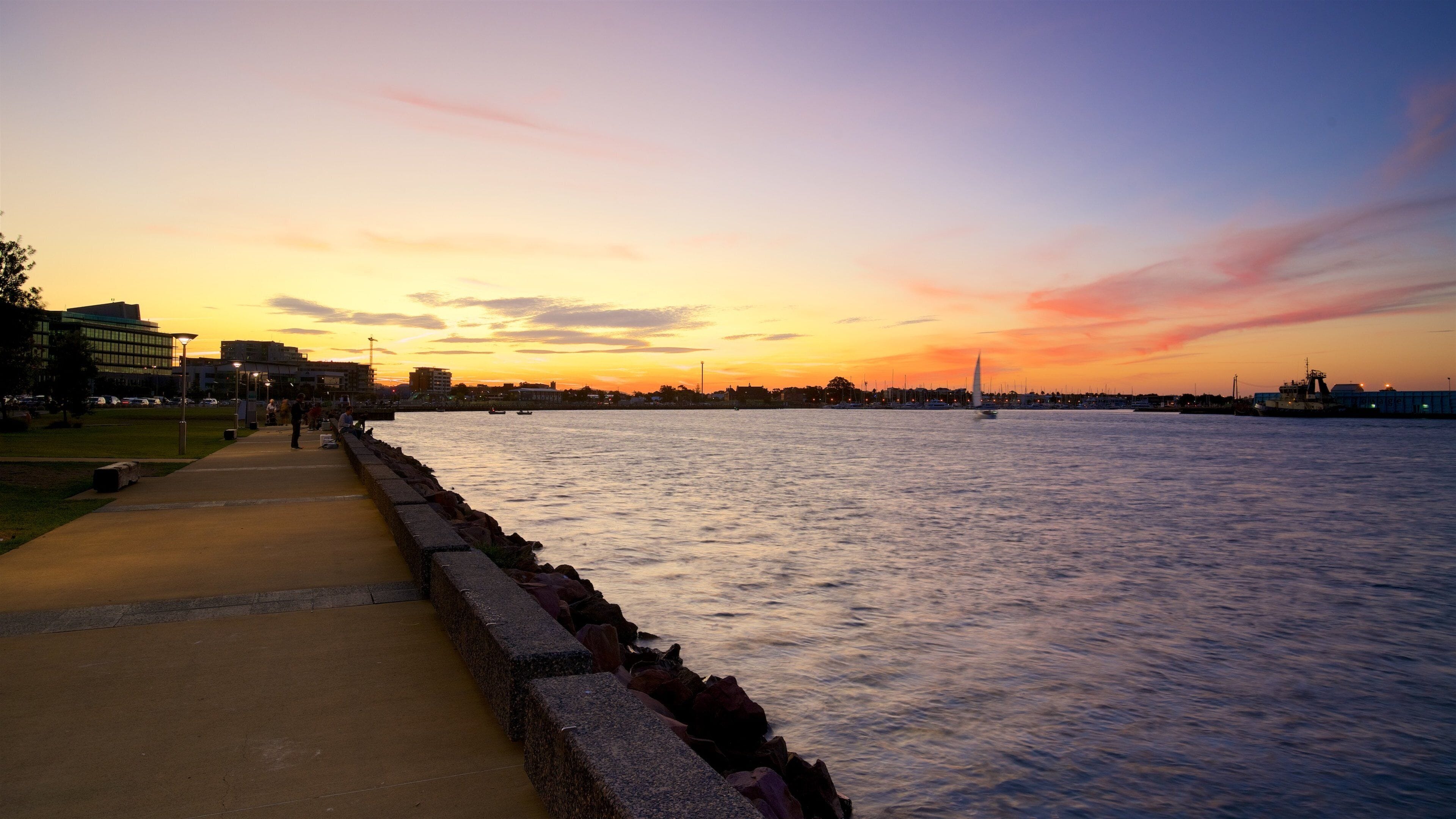 A sunset over a river with a walkway and boats.