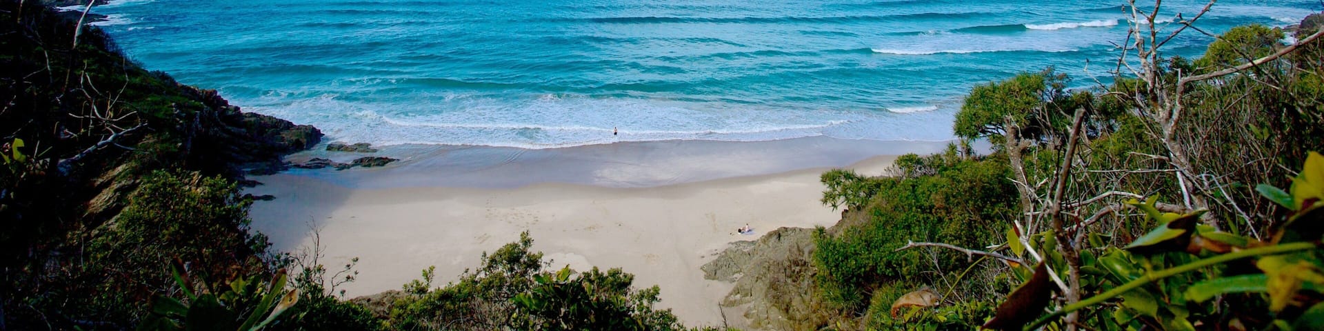 A beach with clear blue water, sandy shore, and rocky cliffs.