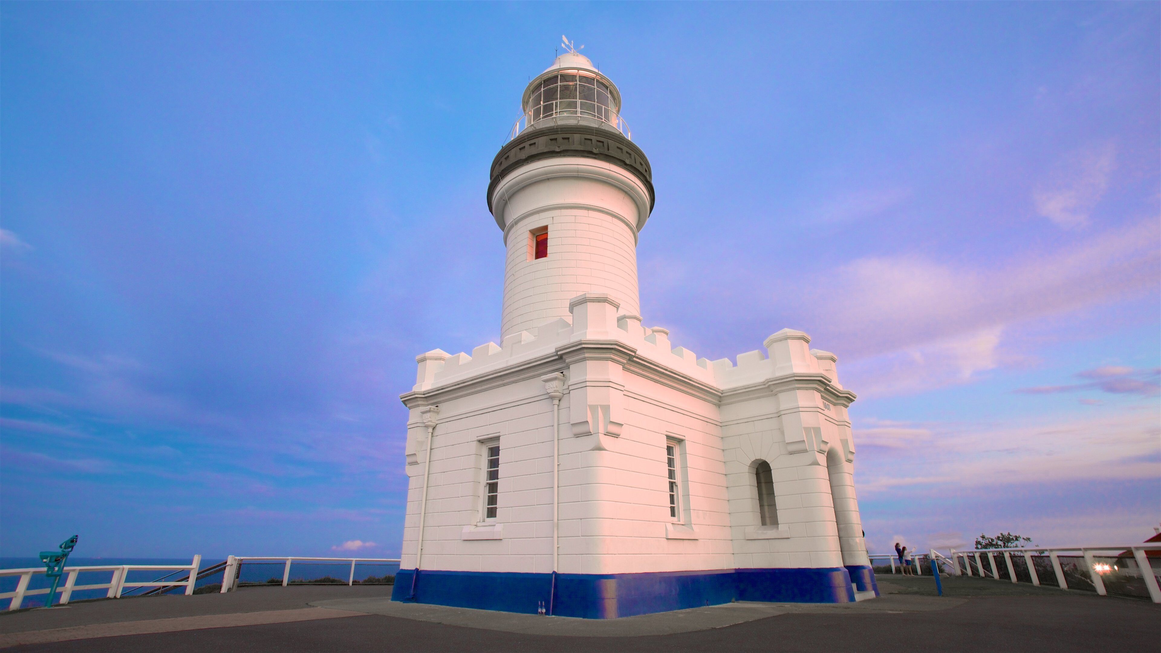 A white lighthouse with a blue base, set against a twilight sky.