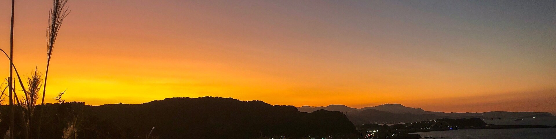 A coastal sunset with a cityscape and mountains in the background.