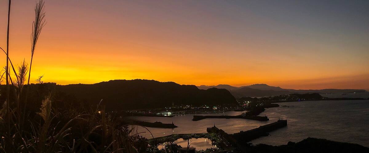 A coastal sunset with a cityscape and mountains in the background.