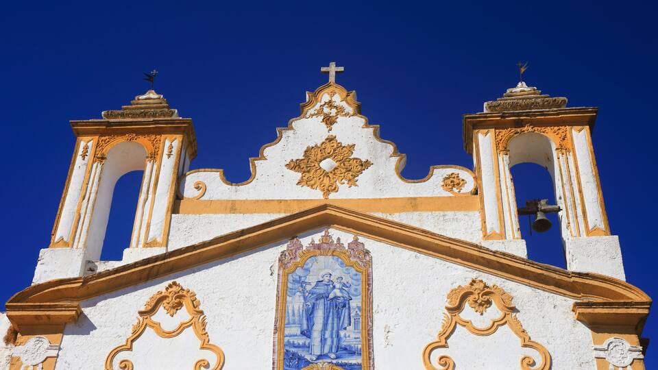 Portugal, Alentejo region, Alter do Chao, Saint Anthony's - Santo Antonio Convent chapel in whitewashed with yellow detailing baroque style against a blue sky. Image of St Anthony in ceramic tiles.