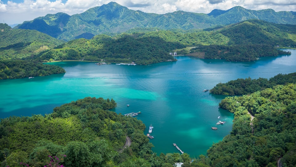 A turquoise lake surrounded by lush green hills and mountains.
