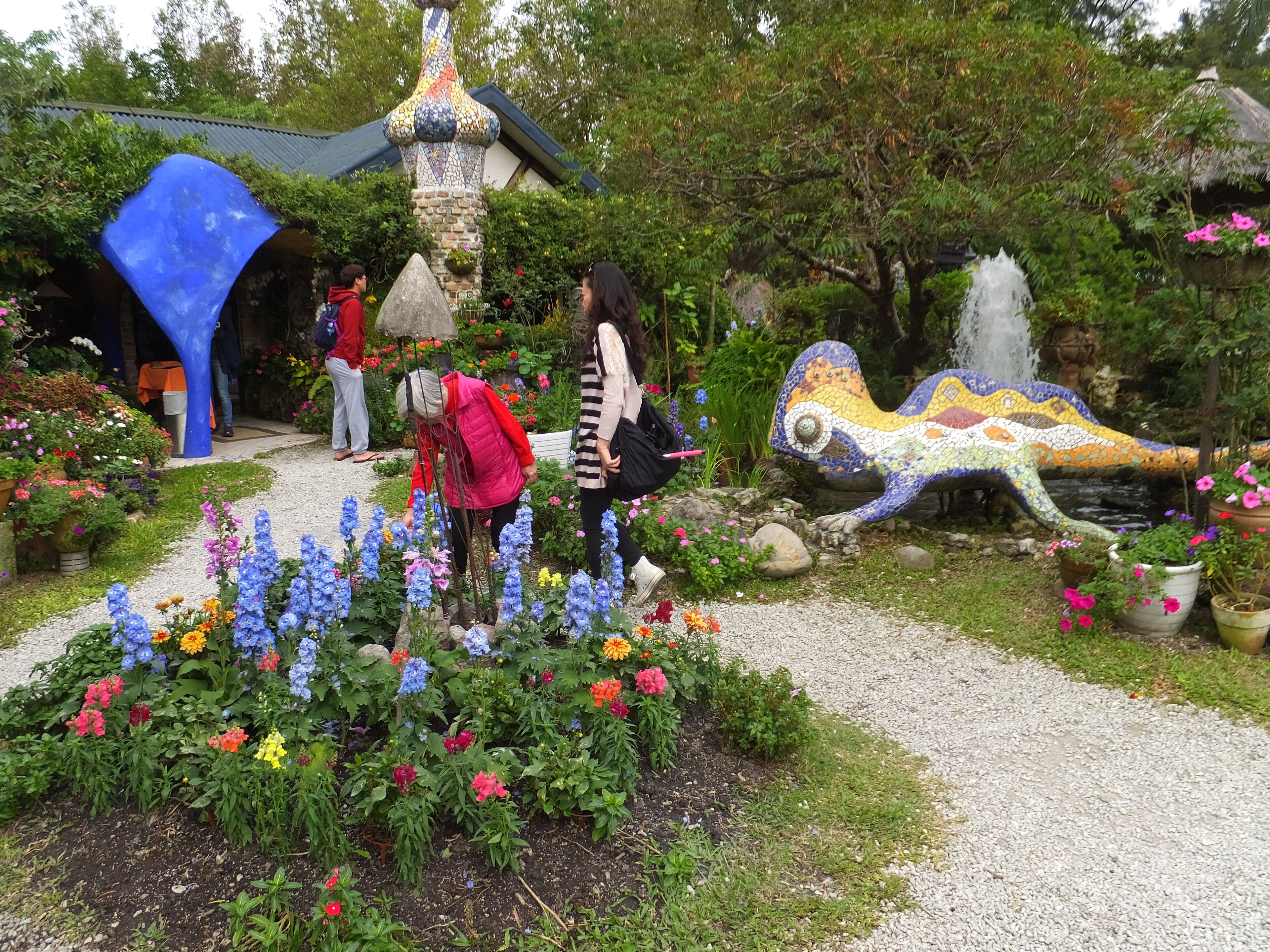 Un jardín con flores coloridas, una escultura de mosaico y un edificio con techo de paja.