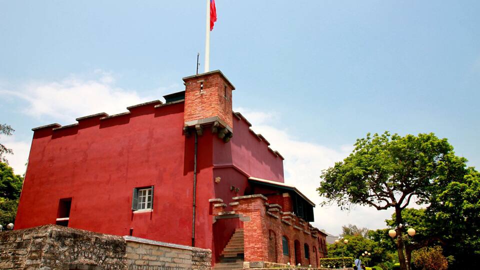 A red building with a flagpole, a staircase, and a tree.