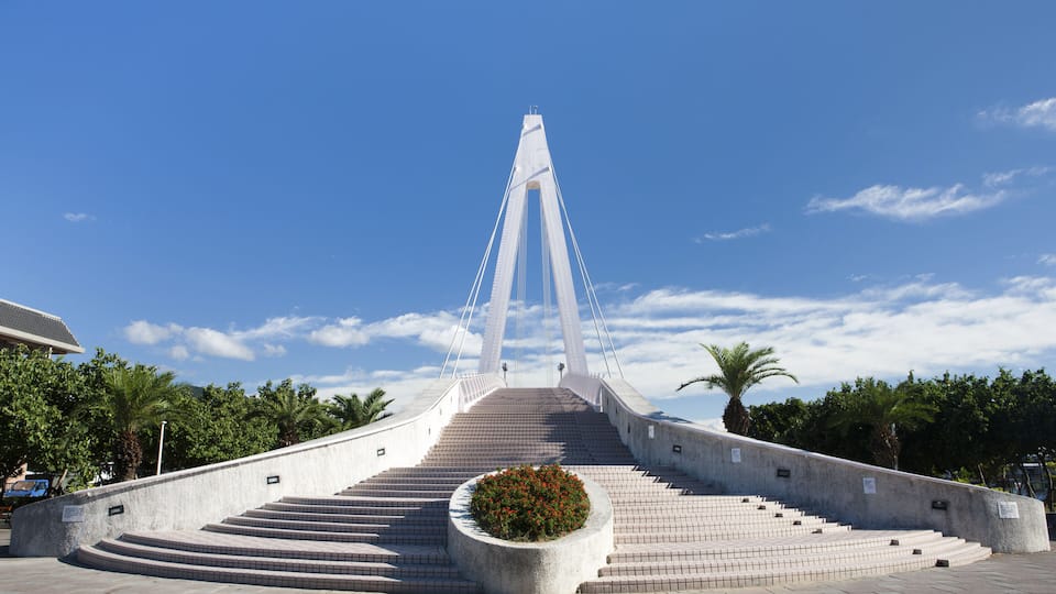 Uma grande ponte com uma torre central e um canteiro circular de flores ao primeiro plano.
