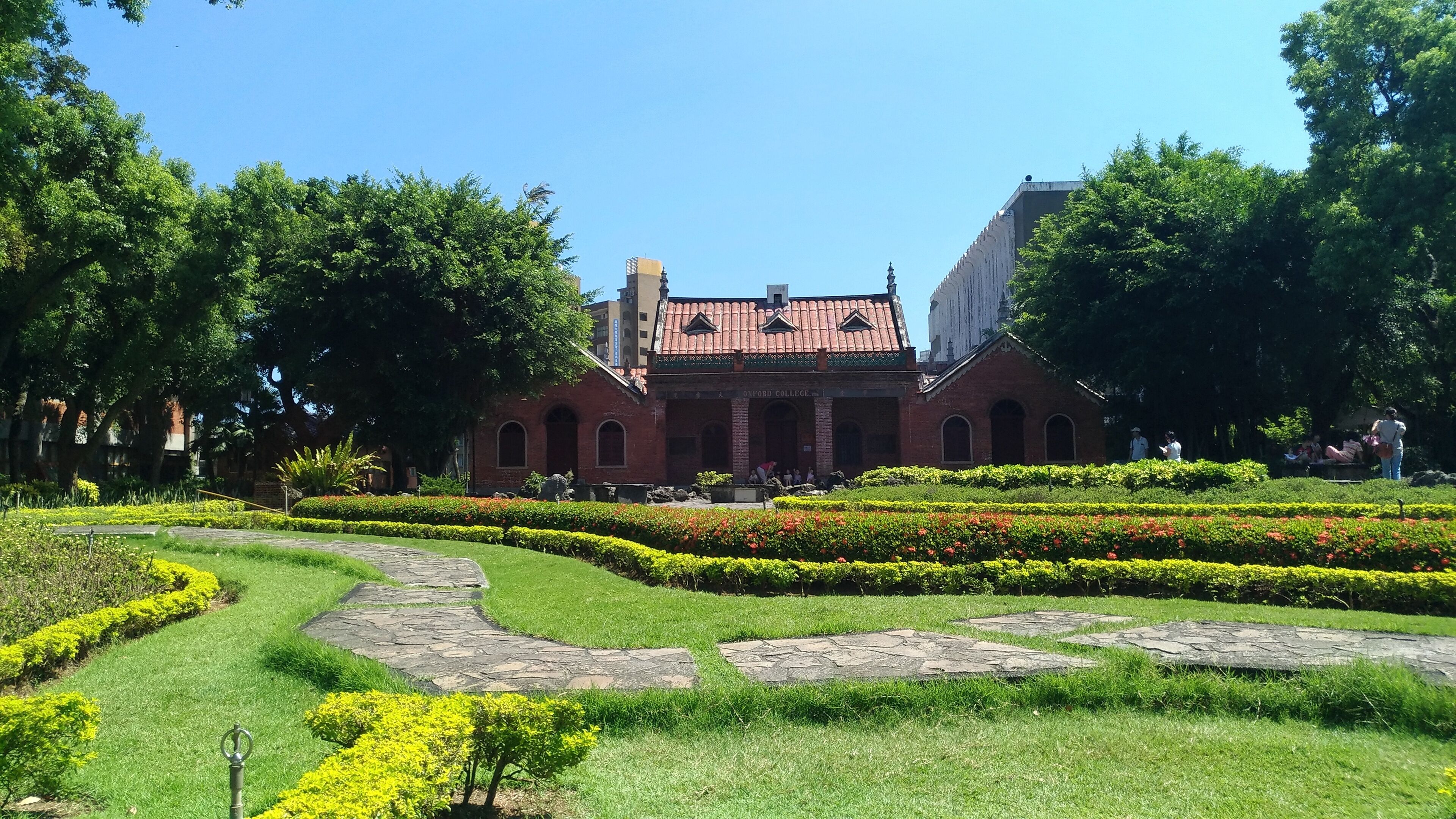 Un edificio histórico con tejado de tejas rojas, rodeado de jardines cuidados y senderos.