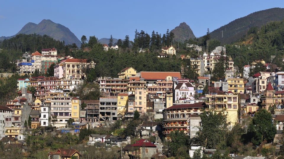 A densely built hillside town with colorful buildings, surrounded by forested mountains.