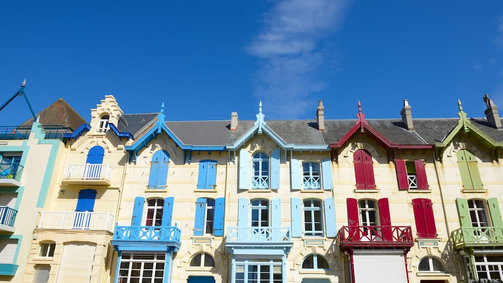 Une rangée de bâtiments aux couleurs vives, avec des volets bleus, rouges et verts, sous un ciel bleu dégagé.
